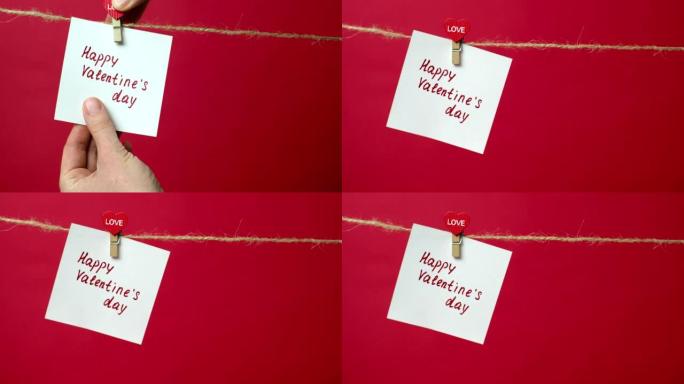 绳子上的纸条特写，上面写着情人节快乐。女孩的手将一张白纸挂在衣夹上的红色背景上。爱情宣言、浪漫关系的