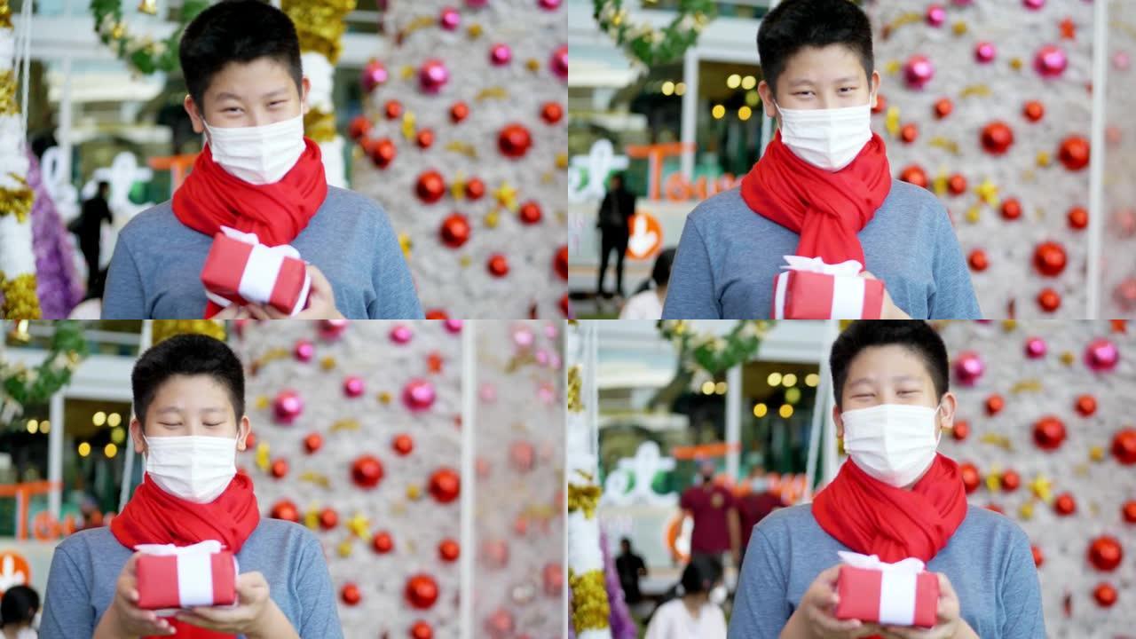 快乐的亚洲男孩戴着口罩，红领巾，拿着红色的礼盒，看着相机和慢动作拍摄。