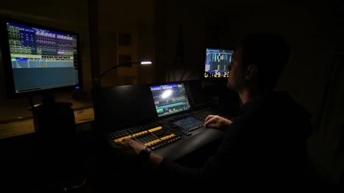 照明工程师在办公室的灯光控制台上工作，俯瞰剧院舞台。