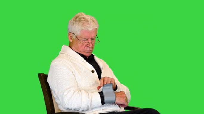老人坐在椅子上，在绿色屏幕上测量血压，色度键