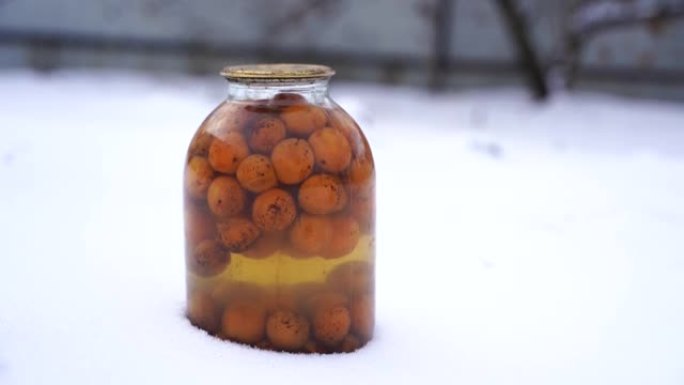 街上雪中水果罐头果汁特写。冬季在花园里密封的蜜饯罐