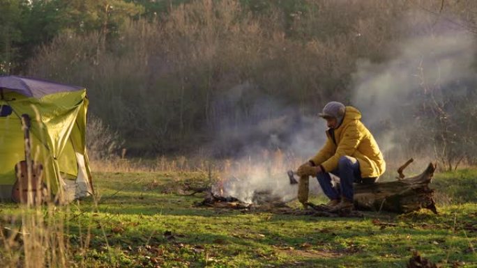 一个年轻人在森林里的火堆附近砍柴