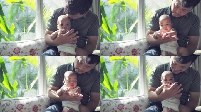 一位亚洲年轻的父亲坐在家里的客厅里，抱着一个孩子和他的男婴玩耍