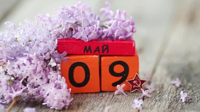 带有俄语文本5月9日的木制日历。胜利日。丁香花瓣落在木制背景上。复制空间。