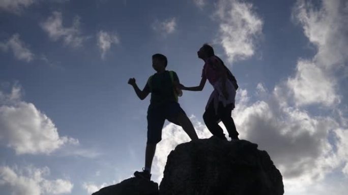 剪影男孩和女孩站在山顶，举手与蓝天，成功的概念。