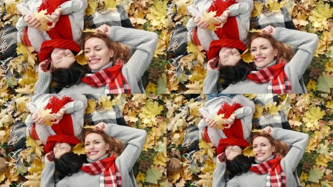 美丽的母亲和可爱的小女儿躺在秋天公园的枫叶中