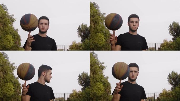 年轻活跃的家伙站在街道篮球场上看着镜头，用手指旋转着球。健康的生活方式和运动理念。特写。慢动作