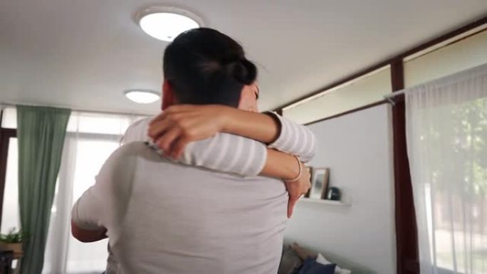 30多岁的年轻成年亚洲男子在家中客厅抱着女人。幸福的夫妇在舒适的房子里兴奋地转身旋转。幸福的关系生活