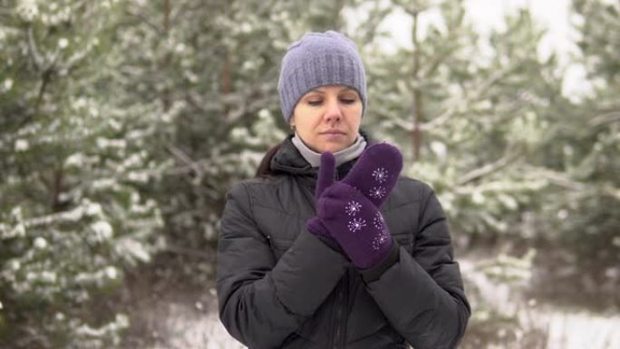 戴着帽子的年轻美女戴上温暖的手套。她站在白雪皑皑的森林里。旅游业。