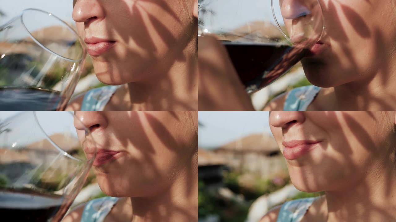 女人在喝酒。女性手的侧视图将装有红酒的玻璃杯带到嘴里，并在大自然的晴天喝。特写