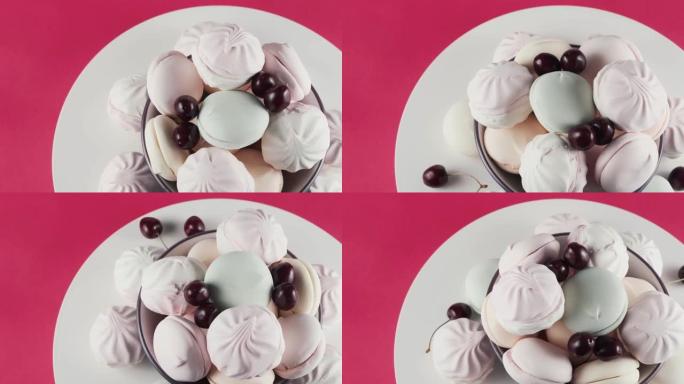 彩色棉花糖和樱桃在粉红色背景上的盘子旋转。