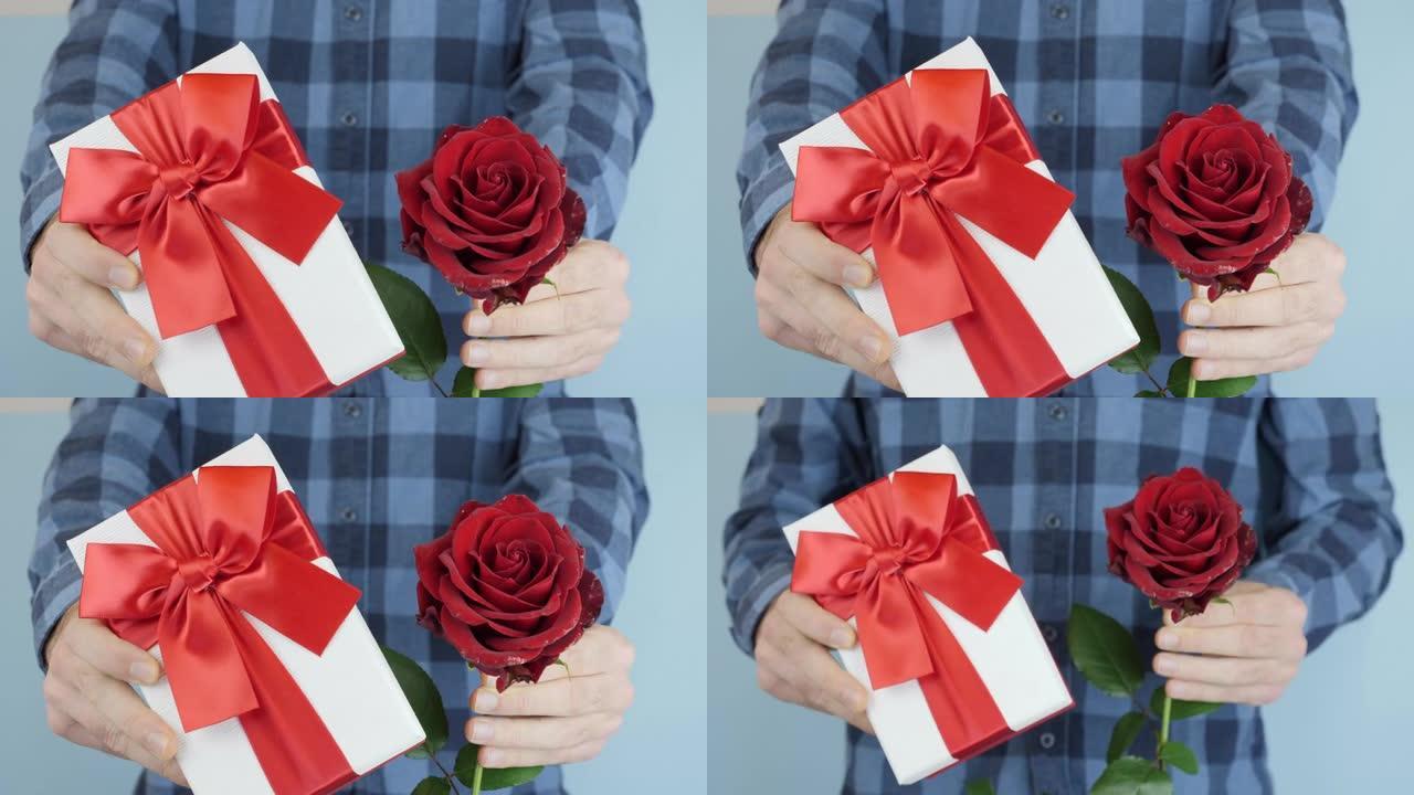 双手将带有红丝带蝴蝶结的礼品盒移向相机，靠近。男人手里拿着情人节礼物。假日概念。男性正在展示绑弓的礼