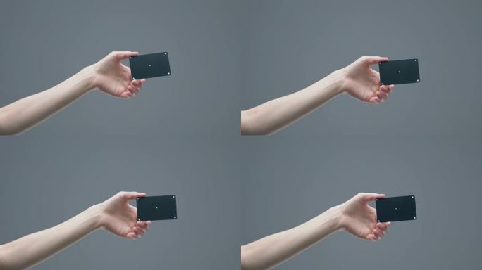 女人的手在灰色演播室背景上显示带有跟踪点的黑色塑料银行卡，广告视频