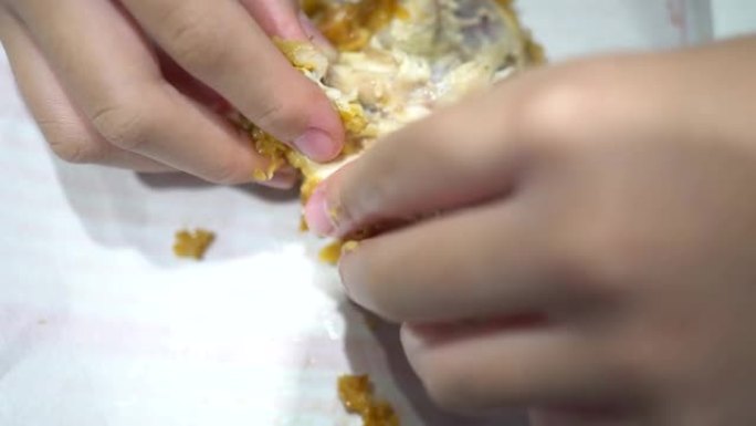 一个小孩在快餐店吃炸鸡。用手把鸡撕开。看过去。