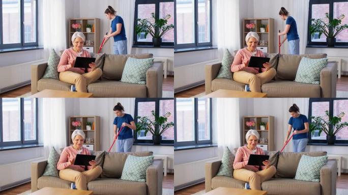 科技、养老、人的概念 -- 幸福的高级女人用平板电脑电脑和管家在家打扫卫生