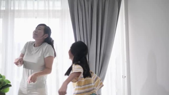 快乐的亚洲单身母亲和女儿一起在家里的窗户附近跳舞，积极的生活方式理念。