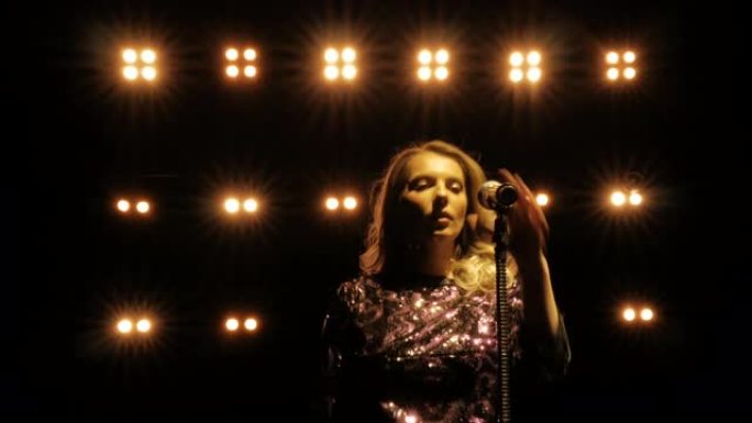年轻的女歌手走到麦克风前，在明亮的黄色灯光下的音乐会上唱歌