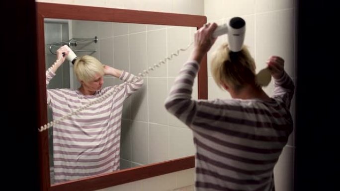 中年金发女子在浴室用吹风机