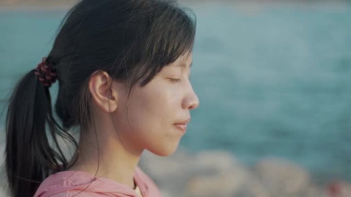 肖像特写年轻美丽的运动女孩训练冥想日落时坐在石头海边。