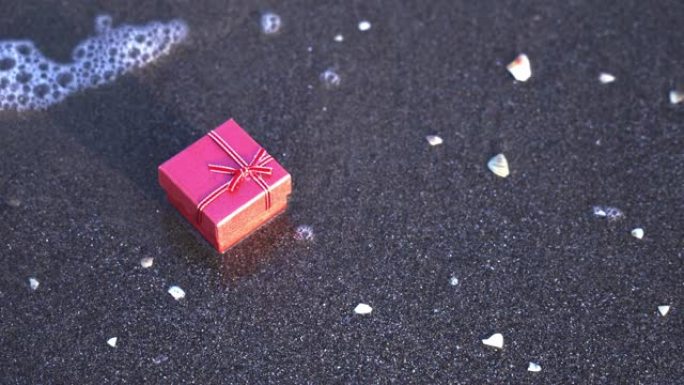 海浪卷到红色礼品盒，缎带和蝴蝶结在沙滩上