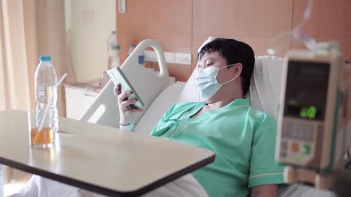 男性亚裔患者在医院病床上用手机发短信。