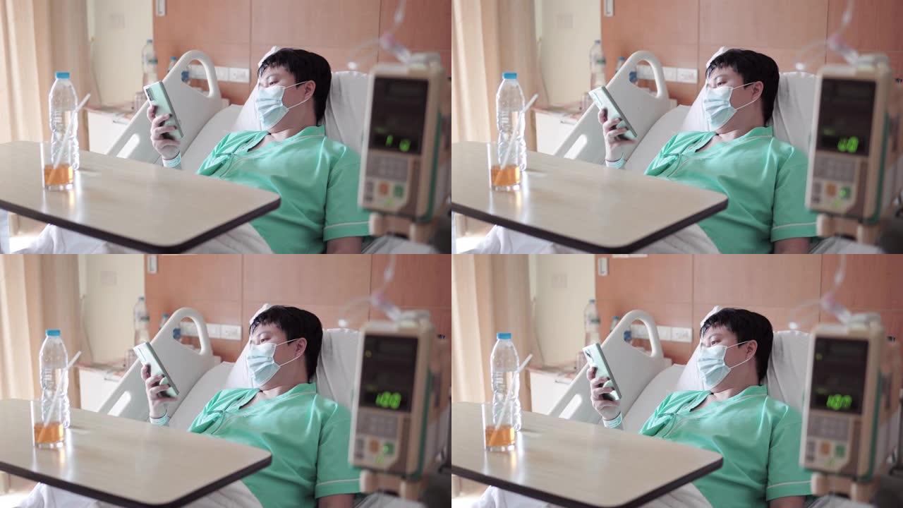 男性亚裔患者在医院病床上用手机发短信。
