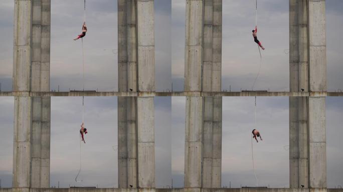 强壮肌肉的马戏团艺术家在空中绳索上表演天空背景上的两个混凝土柱之间的户外，勇气、控制和耐力的概念