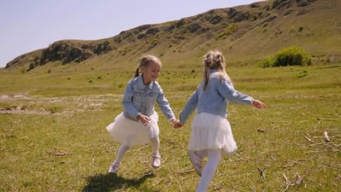 两个开朗的双胞胎姐妹在绿草丛生的田野上手牵手旋转。
