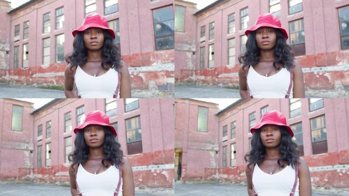 街上年轻黑人女孩的肖像。她表情严肃地站着。戴帽子长发的女孩。
