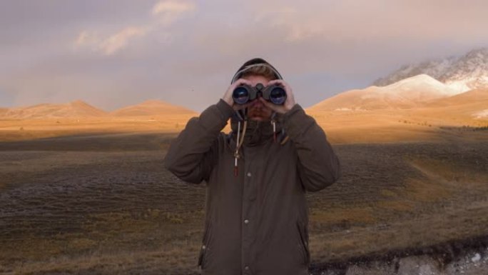 男人用双筒望远镜看，背景是山。