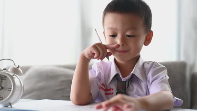 亚洲男孩用心做作业。男孩拿着铅笔写字，男孩在桌子上的白纸上画画，小学和家庭教育，远程在线教育概念。