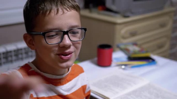 戴眼镜的聪明男孩微笑并谈论他在家里读的书。阅读