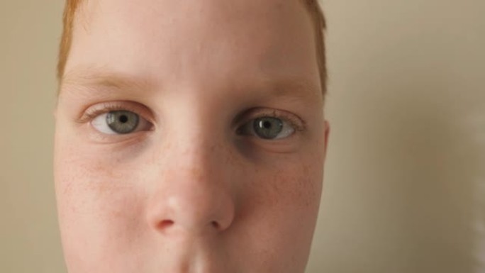红发小男孩的蓝眼睛眨眨眼，看着疲惫的镜头。用雀斑关闭小姜孩子的悲伤凝视。绝望的男孩子的面部表情。