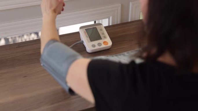 成年妇女在家中在自动血压机上检查血压