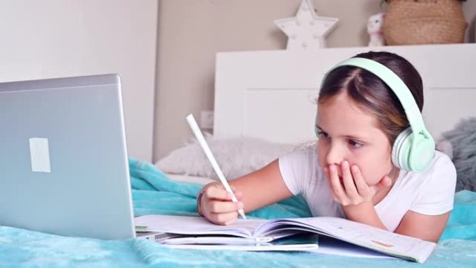 在线课程。一个小女孩，一个戴着耳机的女学生，带着课本，在电脑上上课。检疫时期家庭教育的新版本，cov