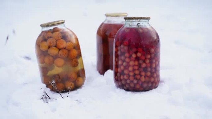 在街上的雪中关闭水果，浆果和西红柿罐头果汁罐头。冬季在花园里密封的蜜饯和腌制蔬菜罐