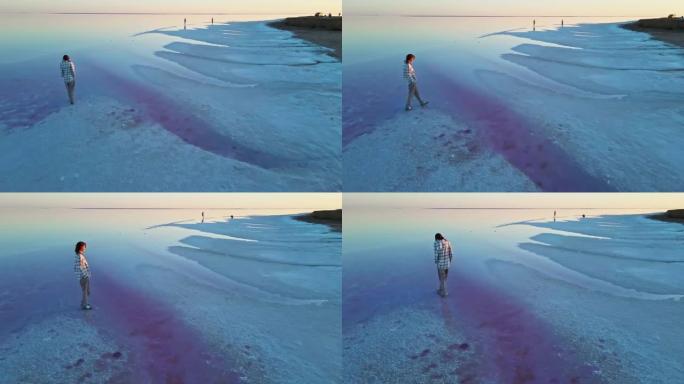 无人机视图年轻女子沿着矿物盐湖的盐海漫步