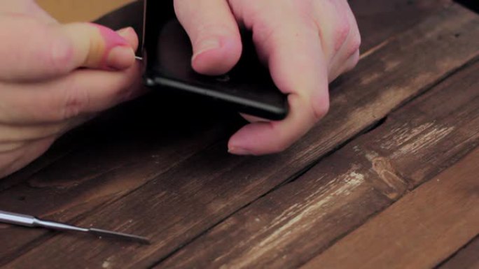 男人的手在木桌上拆卸智能手机。