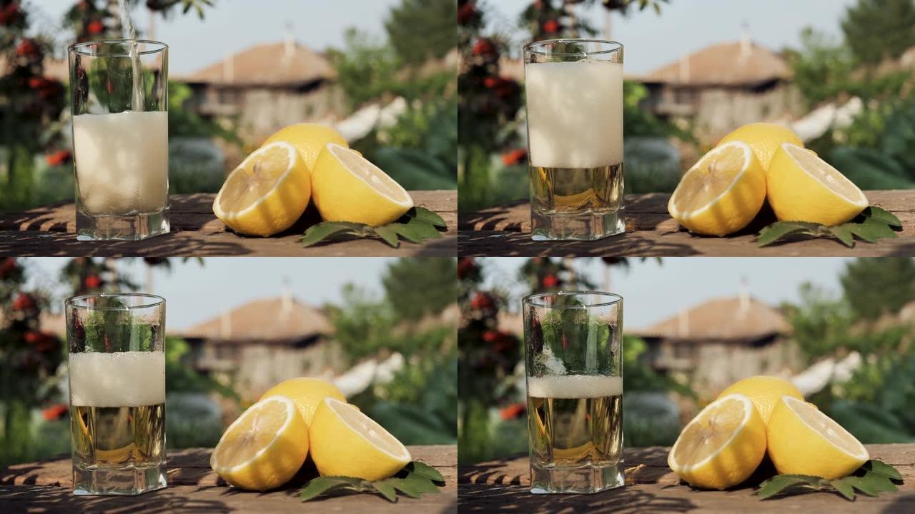 柠檬水倒入玻璃中。在乡间别墅和大自然的背景下，将碳酸柠檬水倒入透明玻璃中，附近有新鲜柠檬。特写