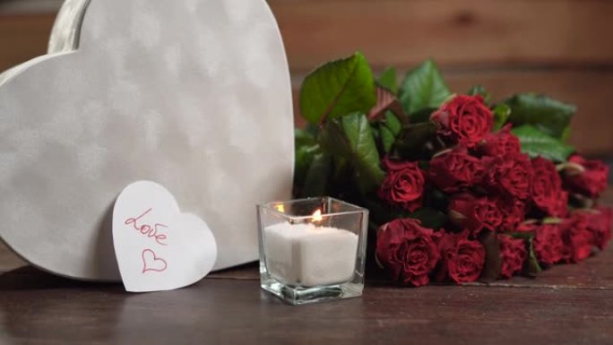 桌子上有一支燃烧的蜡烛，靠近一束玫瑰和一个大的心形盒子。情人与爱的文字。情人节的概念，
