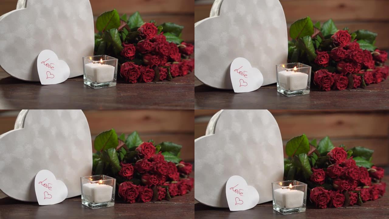 桌子上有一支燃烧的蜡烛，靠近一束玫瑰和一个大的心形盒子。情人与爱的文字。情人节的概念，