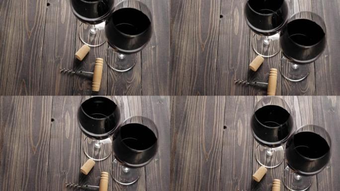 豪华红酒。两个酒杯，一个开瓶器，软木塞和一瓶红酒，由桌上的美味红葡萄制成，背景为黑色。慢动作。顶视图