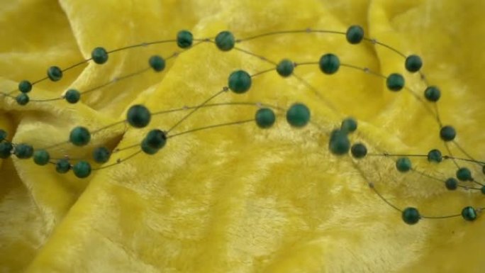 绿色宝石珠宝在黄色柔软的天鹅绒织物上的飞行和波浪运动。