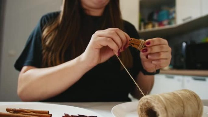 女人用肉桂棒和黄麻做圣诞装饰，把它卷起来。