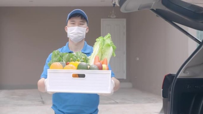 在家庭隔离期间，亚洲送货员戴着口罩和手套，上面装有食品，水果，蔬菜和饮料的食品杂物盒，站在客房门前的