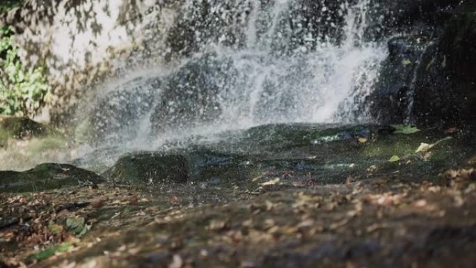 自然界山上的瀑布，溅落在地上，黄色的叶子上，瀑布上的水滴，溪流倾泻在岩石上。