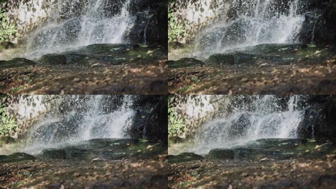 自然界山上的瀑布，溅落在地上，黄色的叶子上，瀑布上的水滴，溪流倾泻在岩石上。