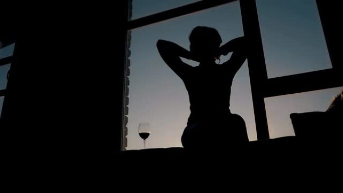 女人的轮廓在窗边的酒杯附近拉直头发