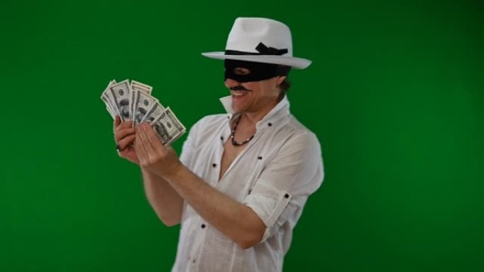 戴着黑色面具和白色帽子的迷人骗子在绿色背景上享受金钱和诱惑。