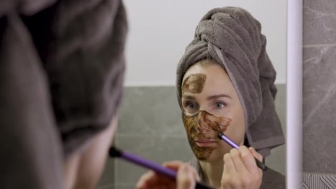 女人在浴室的镜子前用刷子涂泥面膜。护肤美容护理